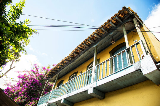 Sobrado com sacada de madeira, portas e janelas de cor azul e paredes amarelas envolvido por arvores e flores. Cidade turística de Embu das Artes, São Paulo, brasil. 