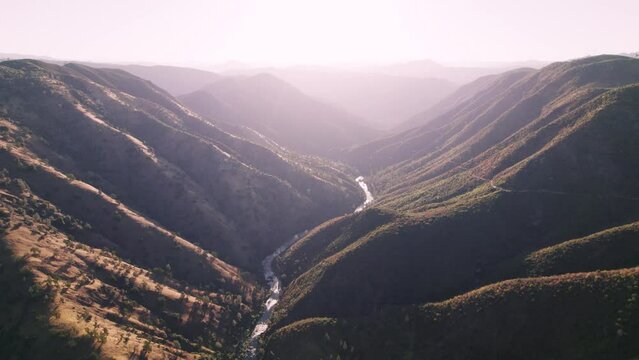 Aerial shot flying high over river with bright sun. Road runs along the mountain range. Shot in California.
