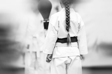 Sports background for martial arts with shallow depth of field and motion blur effect. A girl with a beautiful pigtail from the back in a white kimano with a red belt.
