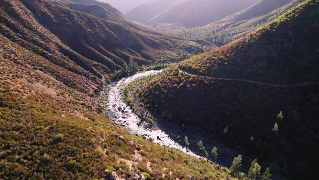 Aerial flying through mountain valley with river and road below, shot in California at sunrise.