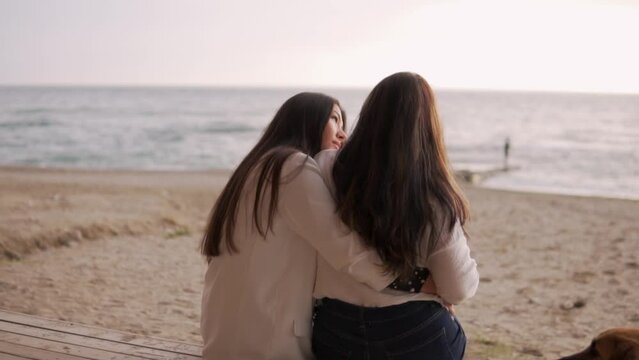 Beautiful daughter hugs her mother in the evening by the sea. View from the back, women with long black hair spend the evening by the ocean. Turkey, Alanya