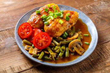 Chicken cutlets with green beans and mushrooms in tomato sauce in a plate decorated with cherry tomatoes.