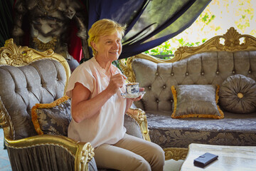 Mature attractive woman traveler sitting alone on the terrace of coffee shop in beautiful park in...