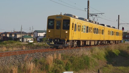 Obraz premium 夕暮れ時の田舎を走る黄色いワンマン電車