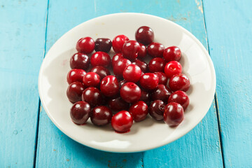 A white plate with cherries on a blue wooden table.