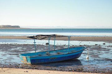 An old fishing boat, without a motor and stranded on the beach during low tide