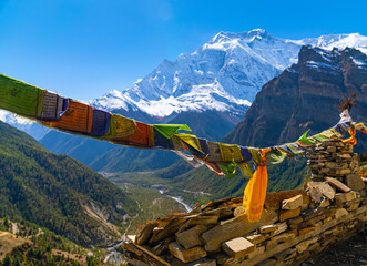 Prayer flags along the Annapurna Circuit Trek with the mountain range in the distance. On a sunny fall cloudless day.