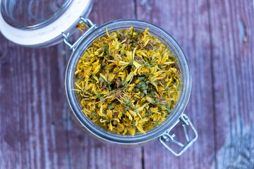 Glass jar full of dry St John's wort or Hypericum perforatum petals on old wood background. St...
