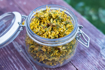 Glass jar full of dry St John's wort or Hypericum perforatum petals on old wood background. St...