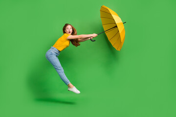 Full body profile photo of impressed girl jump hold umbrella strong wind blowing isolated on green...