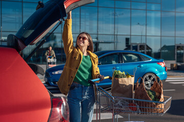 Woman opens car trunk to put groceries from shopping cart © Oleksandr Kozak