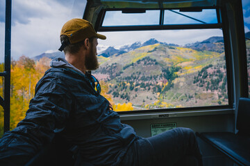 Man riding in a Gondola looking out the window over a scenic landscape of mountains and golden aspens in Telluride, Colorado