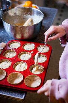 Child scooping muffin batter into baking tin