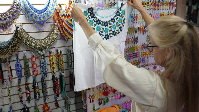Mature woman tourist wearing ethnic clothes looking at locally made blouses in a souvenir shop in Merida, Yucatan, Mexico.
