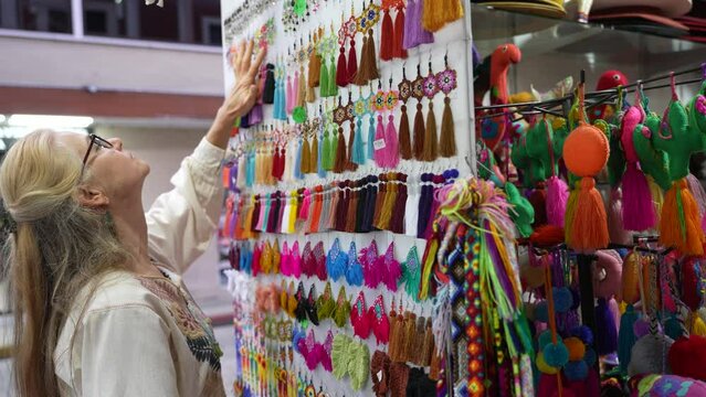 Mature woman tourist wearing ethnic clothes looking at earring souvenirs in a shop in Merida, Yucatan, Mexico.