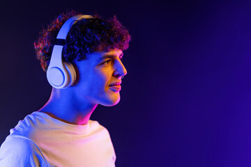 Handsome man listening music with headphones on gradient neon background. Stylish student guy enjoying hit parade on radio.