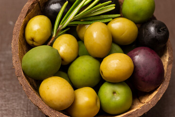 Multi-colored olives and a sprig of rosemary in coconut shell