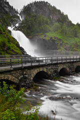 Fototapeta na wymiar Låtefossen waterfall located in Ullensvang Municipality in Vestland County, Norway. The foto shows its right stream of water with the surrounding rocks and greenery as well as the bridge.