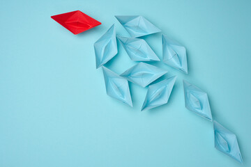 Group of blue paper boats heading in one direction and one red one heading in the opposite...