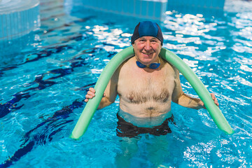 Senior man with a noodle for water gymnastic in the swimming pool. High quality photo