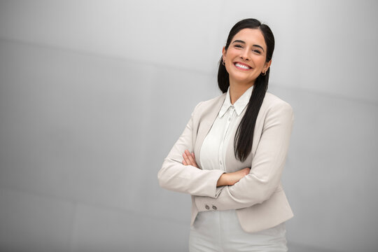 Beautiful hispanic business woman, executive, boss, CEO, entrepreneur in a suit, smiling and standing confidently with arms crossed