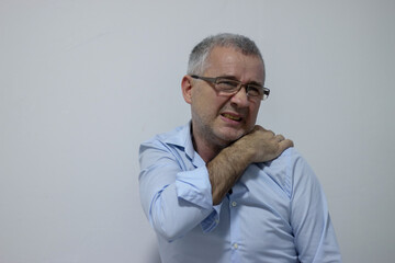 Fototapeta premium Mature man suffering from shoulder and back pain while sitting on chair and working from home. Stressed mature businessman suffering from neck pain and stretching.