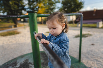 One girl small caucasian child female toddler 18 months old in park play in day on speedy spinner merry-go-round turnabout childhood and growing up concept copy space