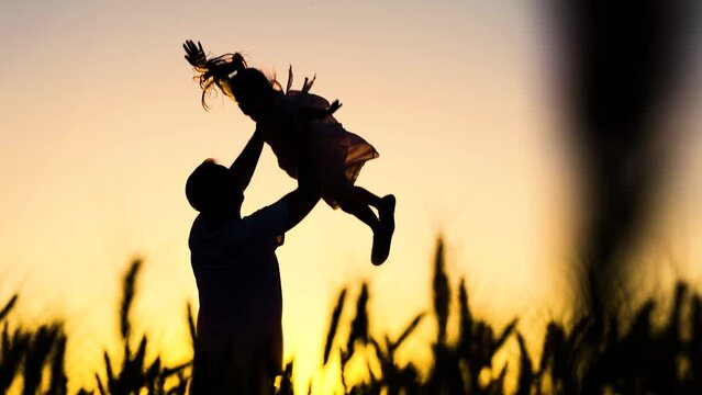 Silhouette, Dad plays with his daughter, throws up child with his hands in sky. Childish, superhero, fly. Family game concept. Happy Father, child, little girl have fun together in park against sun