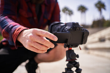Close up view of a man preparing the camera and tripod to record content outdoors.