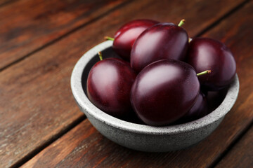 Tasty ripe plums in bowl on wooden table