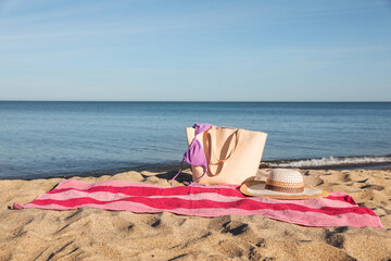 Beach towel with bag, straw hat and bikini on sand near sea, space for text