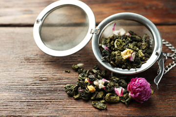 Snap infuser with dried herbal tea leaves and flowers on wooden table, closeup. Space for text