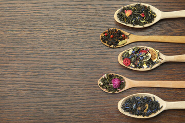 Flat composition with spoons of dried herbal tea leaves on wooden table. Space for text