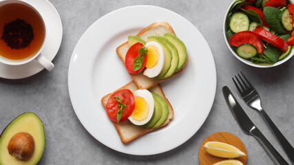 Tasty sandwiches with boiled egg, avocado and tomato served on grey table, flat lay