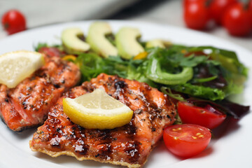 Tasty grilled salmon with lemon and tomatoes in plate, closeup