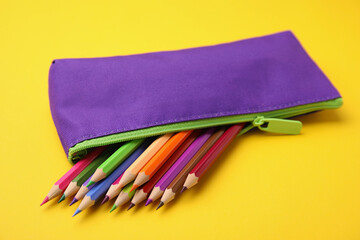 Many colorful pencils in pencil case on yellow background, closeup