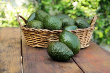 Wicker basket with fresh ripe avocados on wooden table outdoors