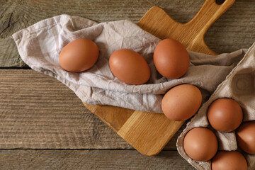Raw chicken eggs with carton, napkin and board on wooden table, flat lay