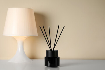 Aromatic reed air freshener and lamp on white table indoors. Space for text