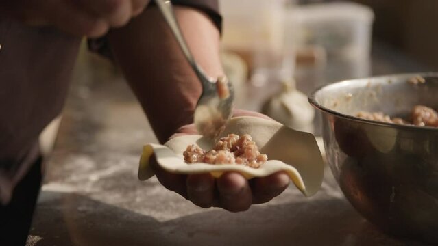 Adding pork meat filling to dumplings, closeup on chef hands