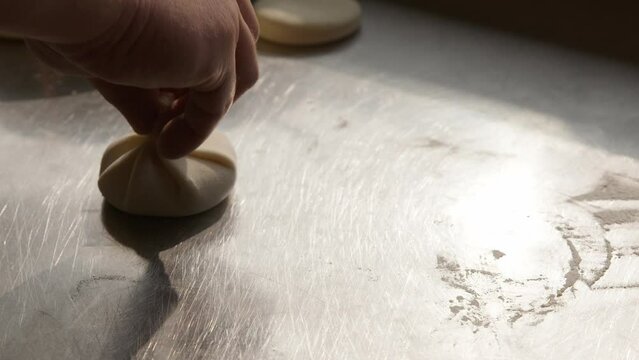 Cook puts raw dumplings on counter top, closeup handheld view