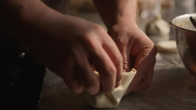 Chef adding fill in khinkali dumplings and rolling them close, closeup on hands