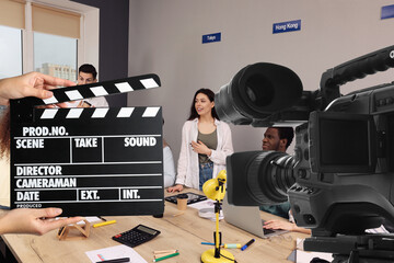 Shooting movie. Second assistant camera holding clapperboard near video camera in front of coworkers (actors) at office (film set) - obrazy, fototapety, plakaty