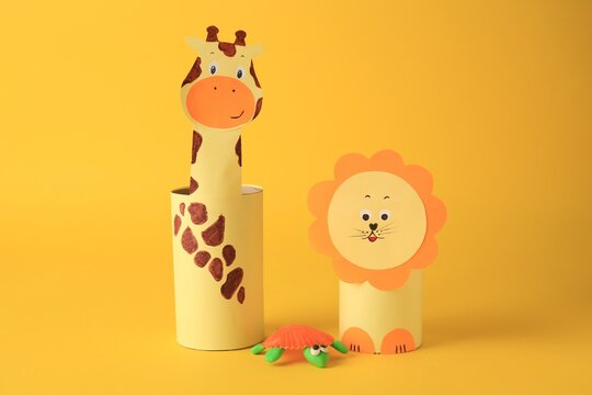 Toy giraffe and lion made from toilet paper hubs with plasticine turtle on yellow background. Children's handmade ideas