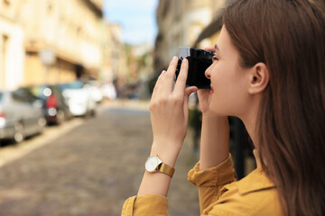 Young woman with camera taking photo on city street, space for text. Interesting hobby