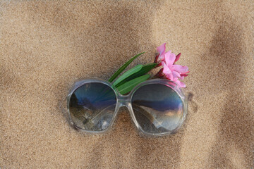 Fototapeta na wymiar Beautiful sunglasses with tropical flower on sandy beach, top view