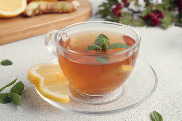 Glass cup of delicious immunity boosting tea with ingredients on light grey table, closeup