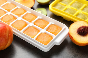 Nectarine and kiwi puree in ice cube tray with ingredients on grey table, closeup