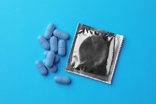 Pills and condom on light blue background, flat lay. Potency problem