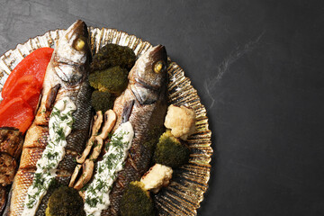Plate with delicious sea bass fish and ingredients on dark grey table, top view. Space for text